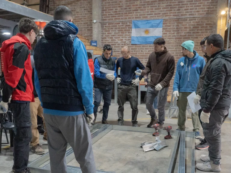 Equipo de participantes alrededor de un panel de steel framing apoyado en el piso, con los planos en la mano