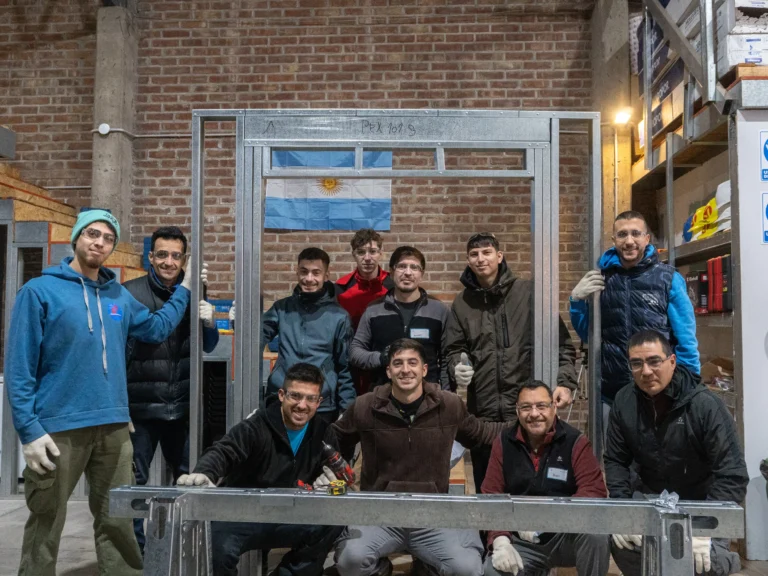 Participantes del taller posan detrás de un panel de steel framing con abertura, armado en equipo